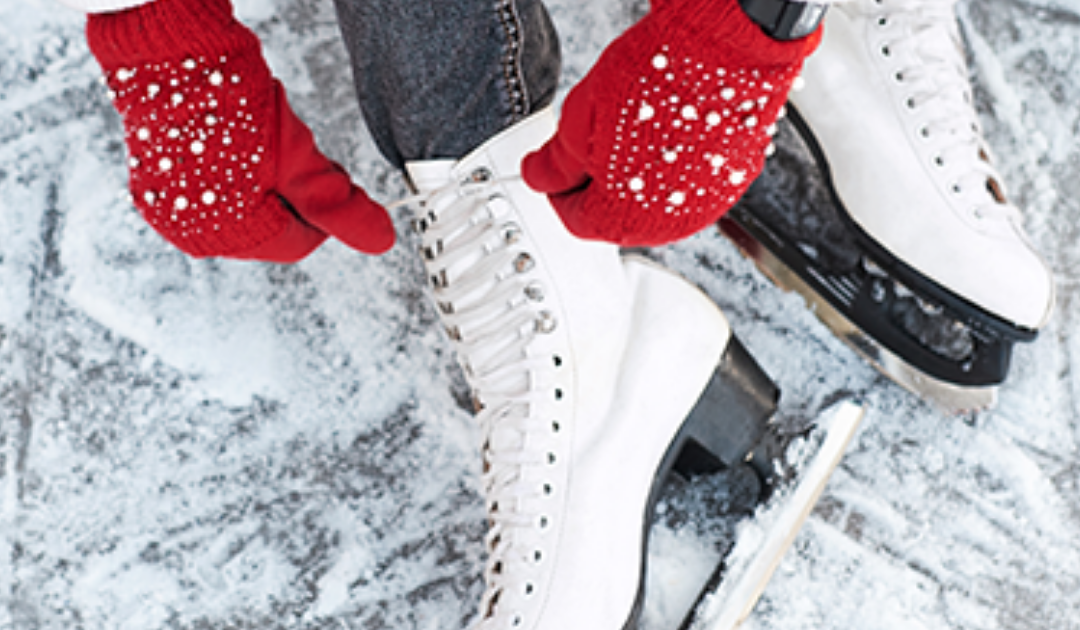 Someone wearing red mittens laces up white ice skates