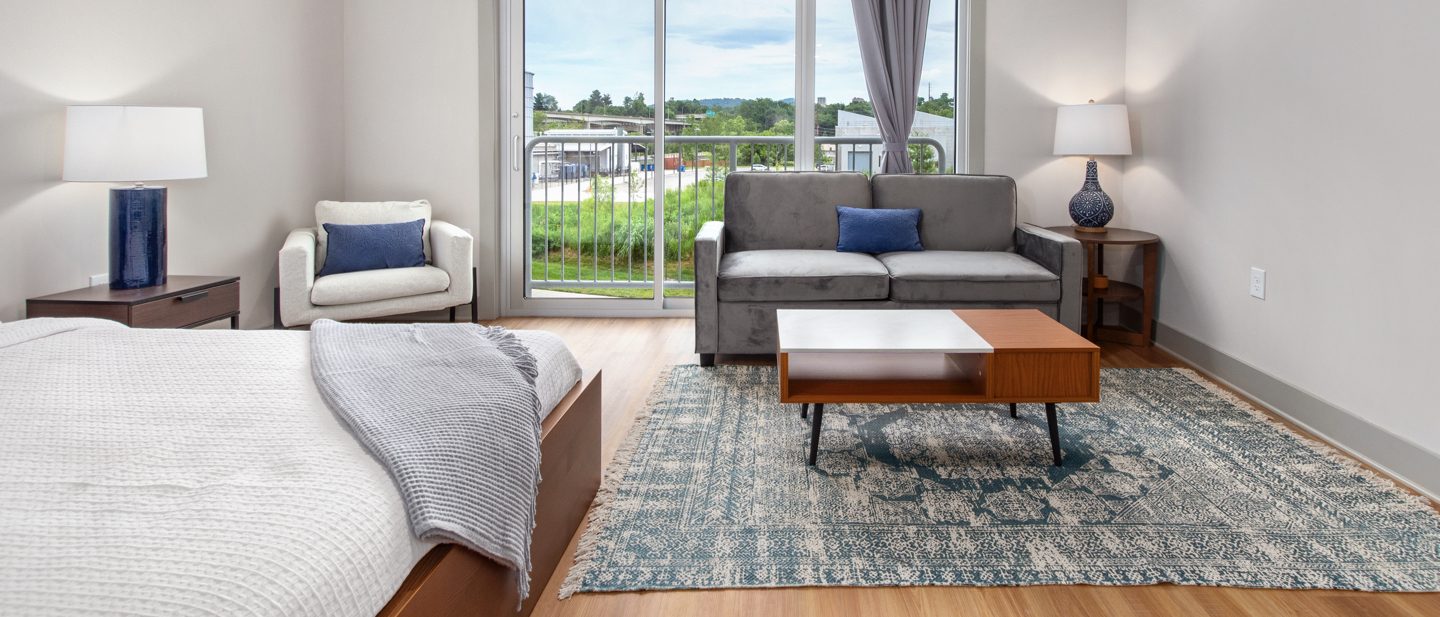 A hotel room with a bed, sofa, coffee table, and balcony door