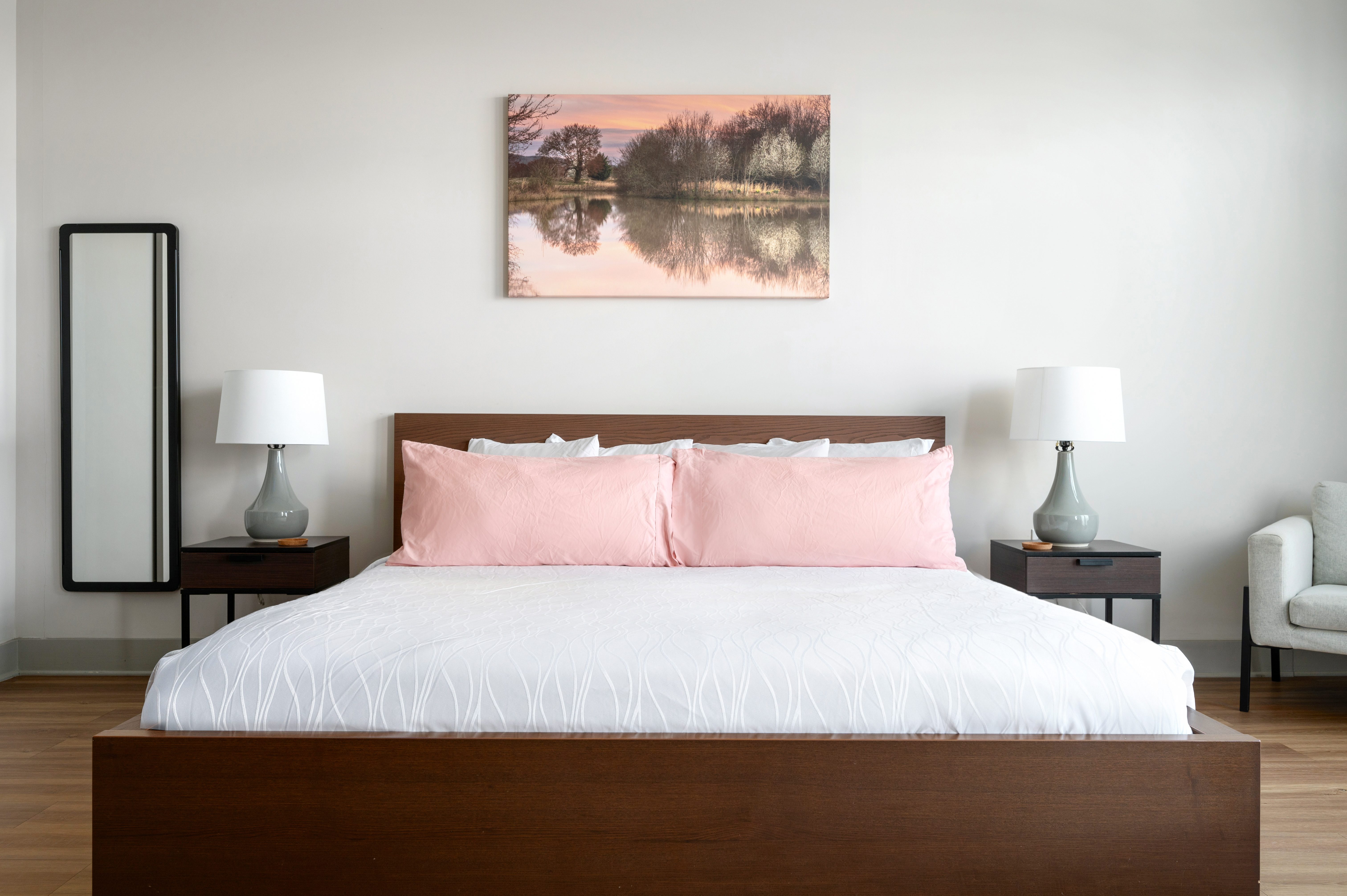 A neatly made bed with pink pillows and a serene landscape painting above it.