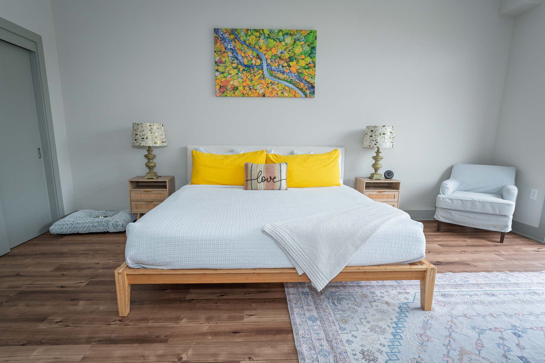 A neatly made bed with yellow pillows and a white comforter in a room with a chair and nightstands.