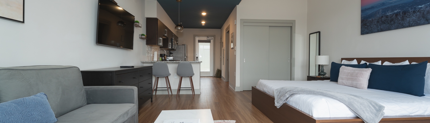 a hotel suite with king bed, full kitchen, grey sleeper sofa and coffee table