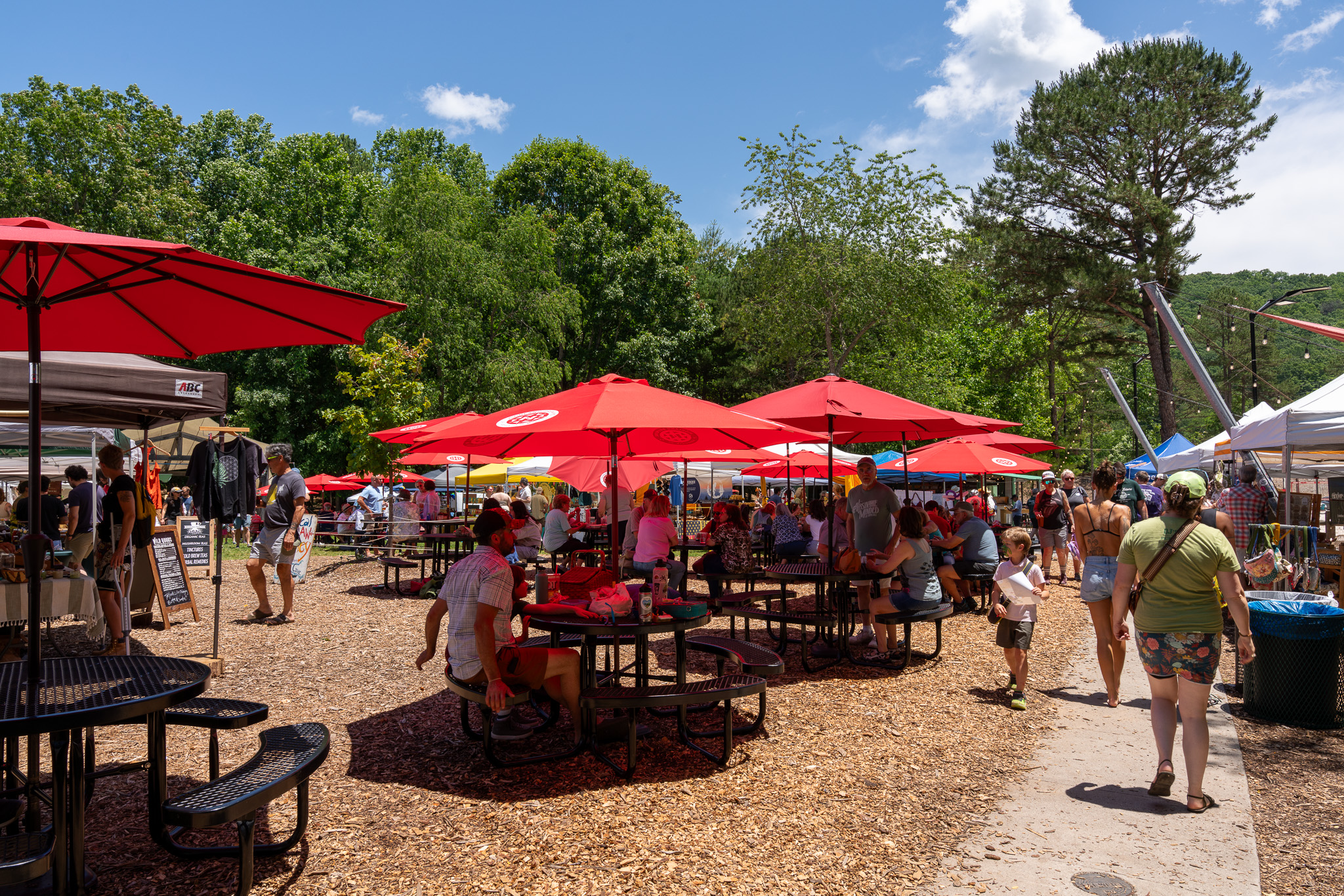 a casual outdoor dining area with red umbrellas and picnic tables