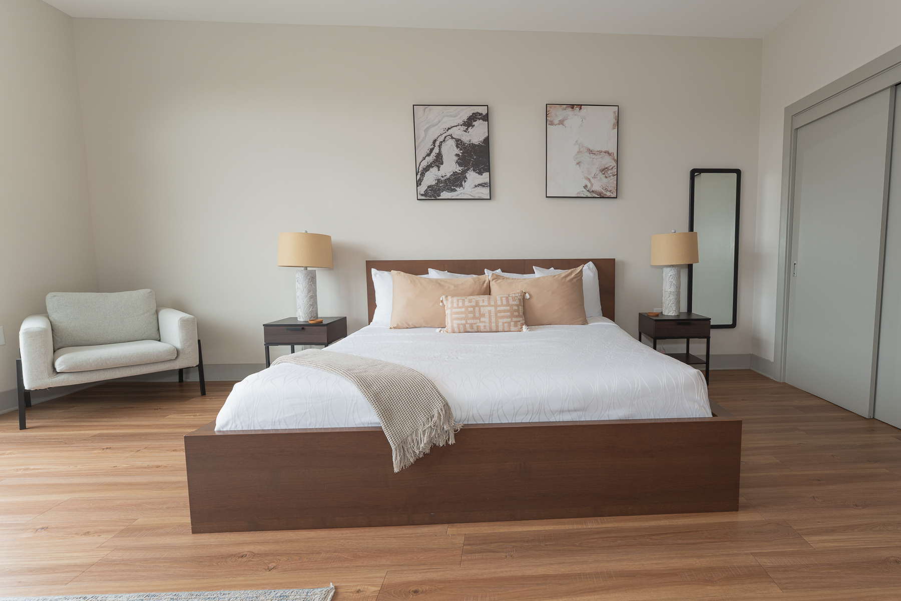 A neatly made bed with pillows and a throw blanket in a room with a chair, nightstands, and artwork.
