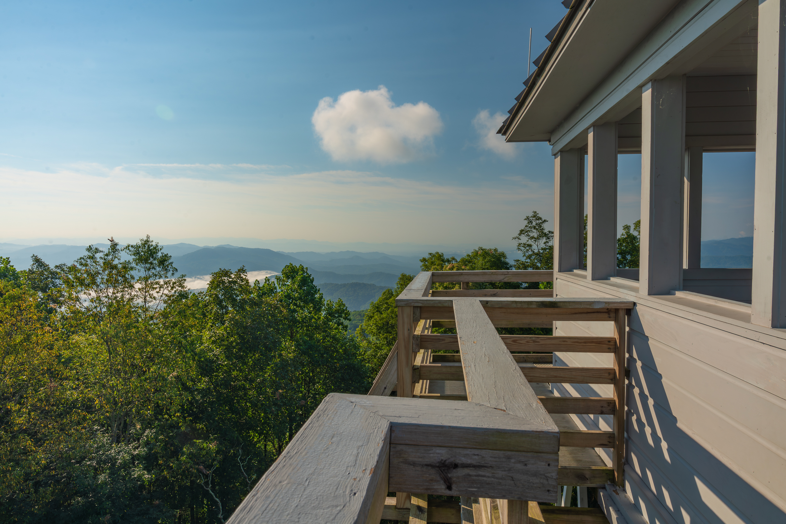 A balcony with a railing overlooking a mountainous landscape with trees and a blue sky.
