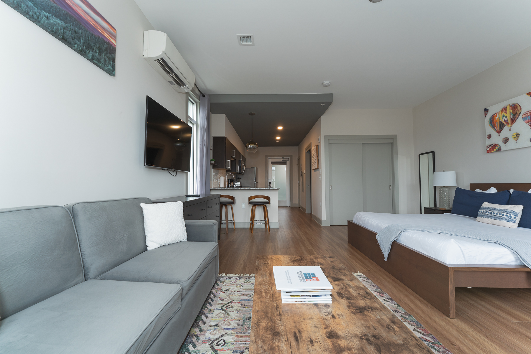 A wide view of a hotel suite with a sofa, bed, kitchenette, and TV.
