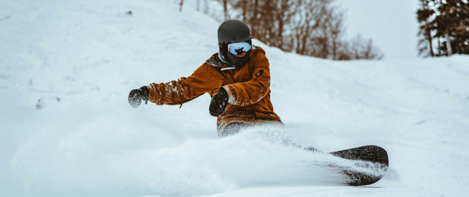 a snowboarder in an orange jacket, goggle and a helmet rides down a snowy slope.