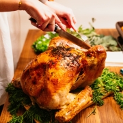 A woman carving a thanksgiving turkey with green herbs and casseroles in the background.