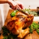 A woman carving a thanksgiving turkey with green herbs and casseroles in the background.