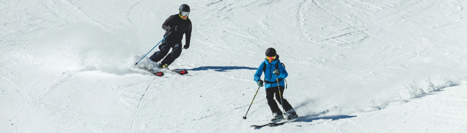 Two skiers carving down a sunny, groomed slope on a winter ski day near Asheville